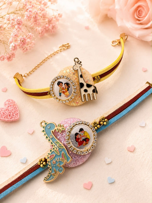 Two personalized Rakhi bracelets styled on a soft pink background with decorative flowers and heart confetti. One bracelet is gold with a giraffe charm and a photo oval; the other is pink with a blue and gold bird charm and a photo oval.