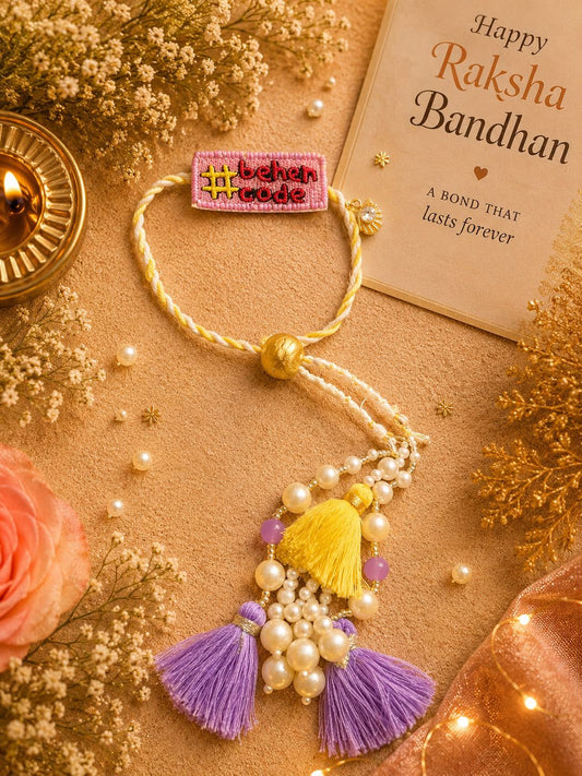 A decorative Rakhi bracelet laid flat on a warm beige surface with floral props and a card reading 'Happy Raksha Bandhan.' The bracelet has a cream braided cord, a pink embroidered patch with yellow text, white faux pearls, a yellow tassel, and purple tassels.