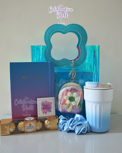 Collection of items including a blue mug, gift card, and small bag on a white surface with 'The Celebration Shelf' branding.