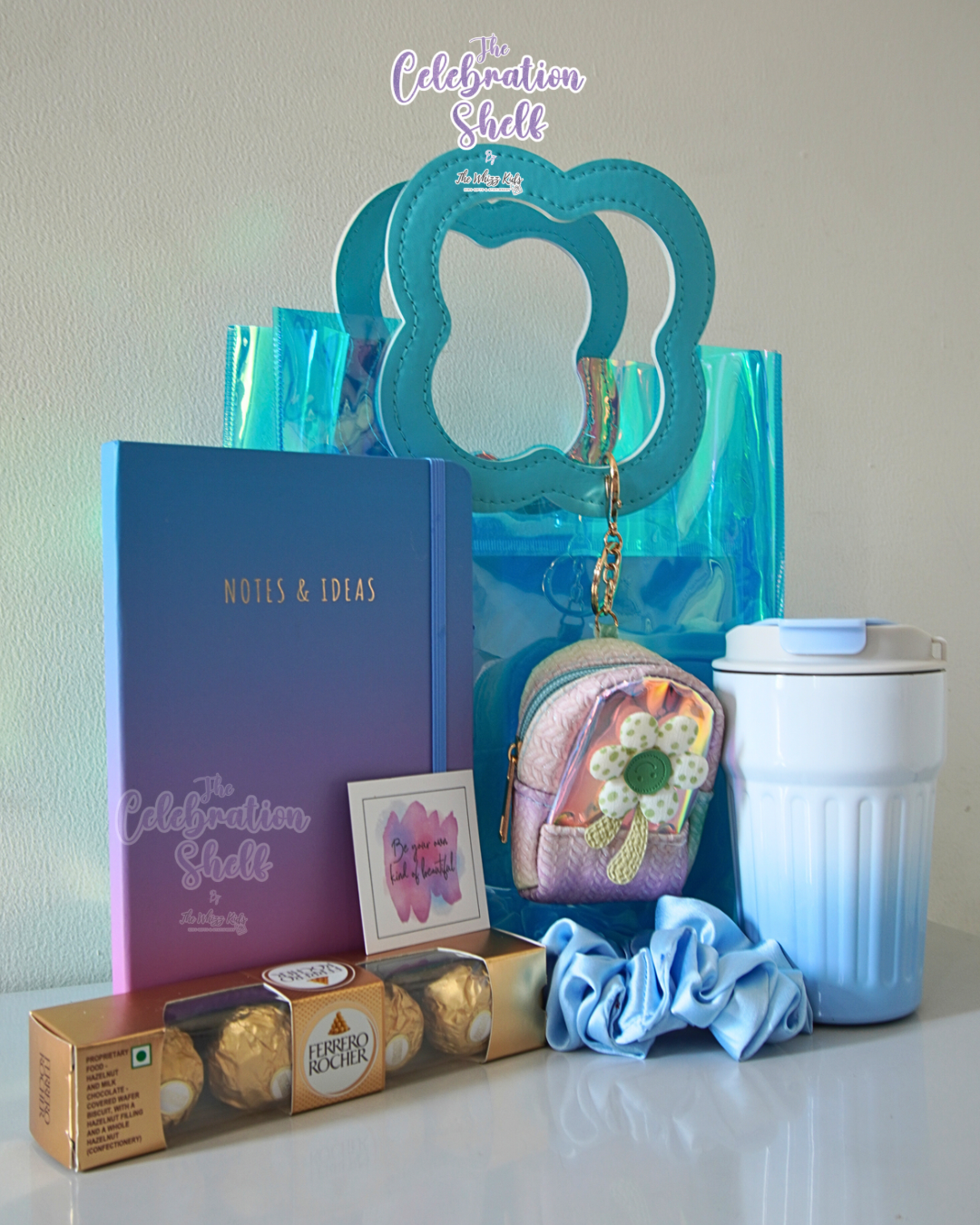 Collection of items including a notebook, chocolate box, and decorative items on a white surface with 'The Celebration Shelf' branding.