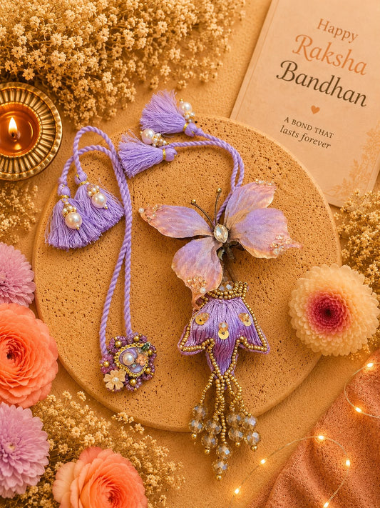 A decorative Rakhi with a purple butterfly and floral design, displayed on a cork coaster with a lit candle, dried flowers, and a Raksha Bandhan greeting card.