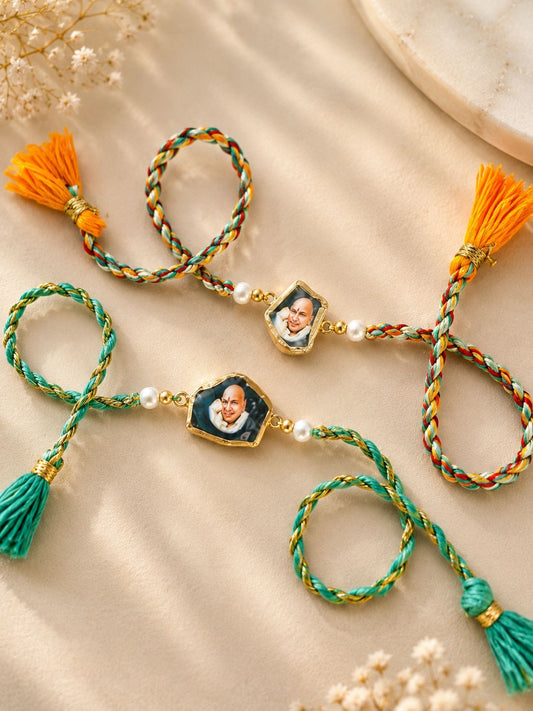 Two braided string ornaments with tassel ends and small portrait charms, arranged on a beige fabric background with decorative dried flowers and a marble-like prop.