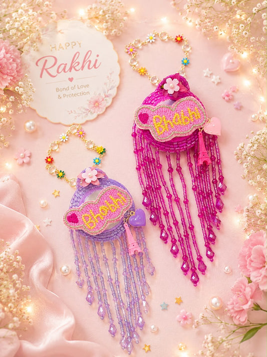 Two handmade Rakhi beaded wristbands with long dangling tassels, one in purple and one in magenta pink, both featuring embroidered 'Bhooth' text. They are displayed on a soft pink background decorated with flowers, pearls, and fairy lights, alongside a 'Happy Rakhi' card.