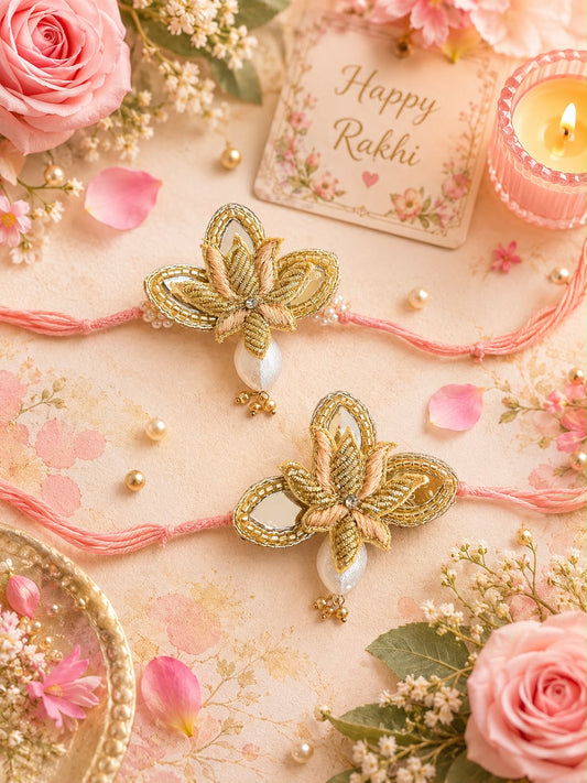 Two decorative Rakhi threads with gold butterfly-shaped ornaments and white pearl drops, arranged on a pink floral surface with roses, flowers, a lit candle, and a card that reads Happy Rakhi.