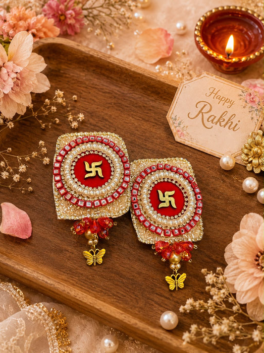 A pair of traditional Indian Rakhi earrings displayed on a wooden tray, surrounded by decorative flowers, pearls, a lit diya, and a 'Happy Rakhi' card.