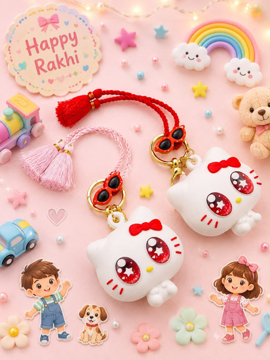 Two cute 3D Hello Kitty keychains with red tassels and gold rings, displayed on a pink background decorated with festive Rakhi-themed props like a rainbow, teddy bear, and flowers.