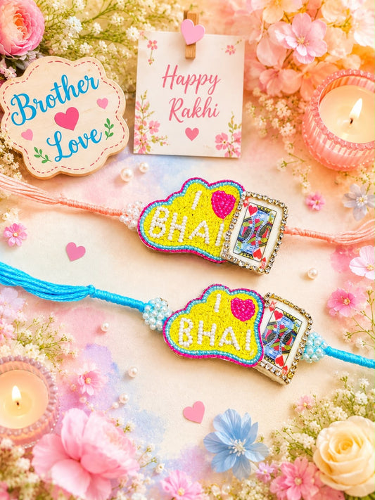 Two handmade Rakhi bracelets with 'I [heart] BHAII' cloud-shaped charms are displayed on a decorated flat-lay background with flowers, candles, and a 'Brother Love' and 'Happy Rakhi' card.