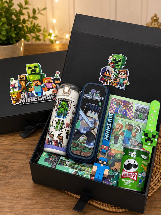 A Minecraft-themed gift set displayed in an open black box on a wooden surface. The set includes a white insulated bottle with green Creeper graphics, a dark blue Minecraft-themed pen or pencil case, a green wrist strap, a green drink can, and a small printed card or notebook, plus matching stickers on the box lid.
