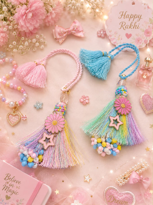 Two decorative tassel keychains or bag charms styled on a soft pink background with floral props, beads, and pastel accessories. The left tassel is pink with multicolor fringe and a pink flower detail; the right tassel is blue with pastel green, yellow, and purple fringe, beads, and a star charm.