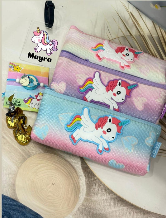 Three pastel zippered pencil cases with cartoon unicorn designs are arranged on a light surface with decorative props including a seashell, dried leaves, and a small card labeled Mayra.