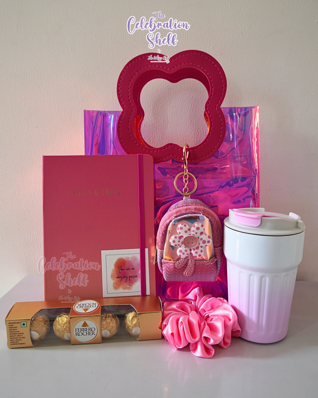 Collection of pink-themed items including a keychain, scrunchie, and tumbler on a white surface with 'The Celebration Shelf' branding.