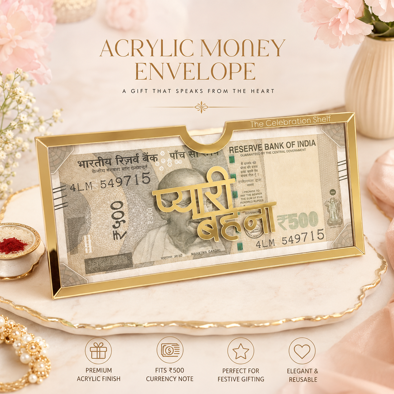 Gold acrylic money envelope styled with a replica Indian 500 Rupee note inside, presented on a decorative tray with pink flowers and text reading 'ACRYLIC MONEY ENVELOPE' and 'The Celebration Shell'.