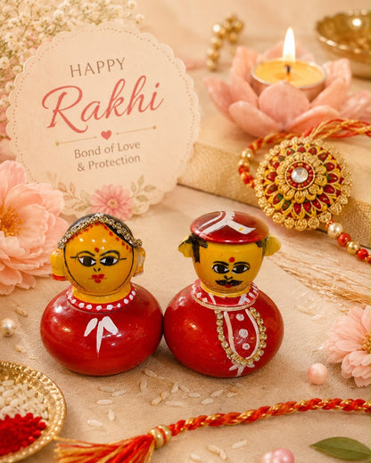 A festive Rakhi-themed flat lay featuring two hand-painted wooden dolls, a red and gold Rakhi, a pink lotus flower, a lit tealight candle, and a round card that reads 'Happy Rakhi - Bond of Love & Protection' on a beige surface with scattered rice and decorative elements.