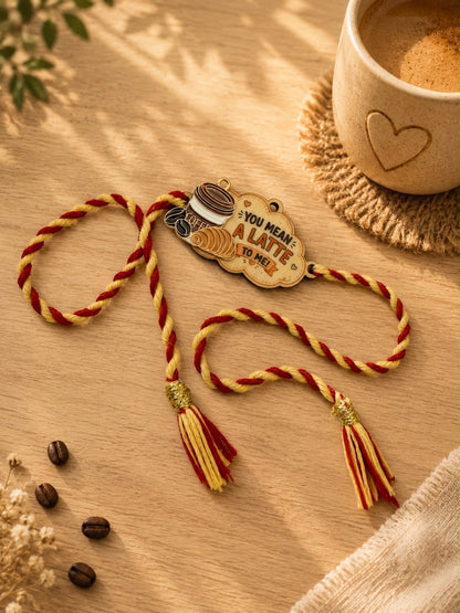A decorative braided cord ornament with a wooden tag that reads 'YOU MEAN ALATE TO ME!' and small coffee-themed illustrations, styled on a wooden surface with coffee beans, a cup of coffee, and soft shadows.