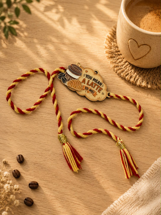 A decorative braided cord ornament with a wooden tag that reads 'YOU MEAN ALATE TO ME!' and small coffee-themed illustrations, styled on a wooden surface with coffee beans, a cup of coffee, and soft shadows.