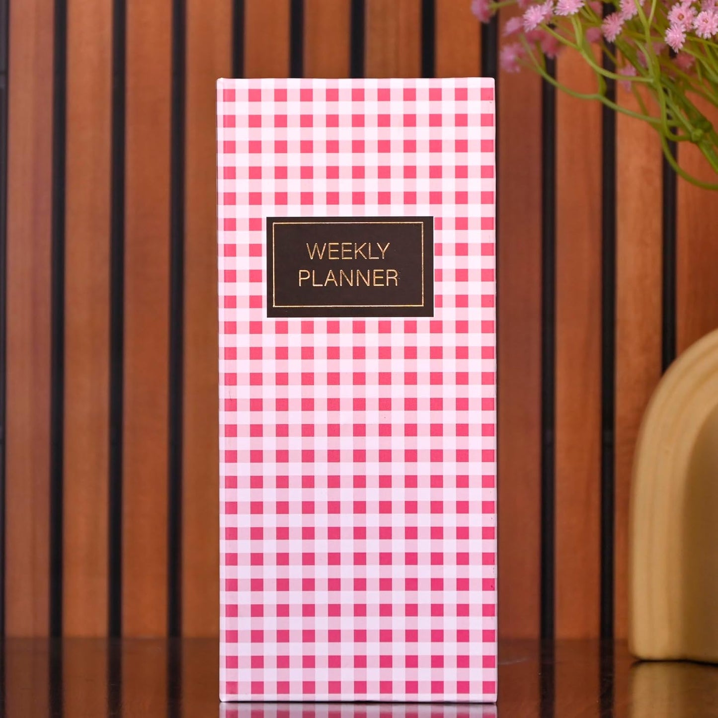Weekly planner with pink checkered design on a wooden surface