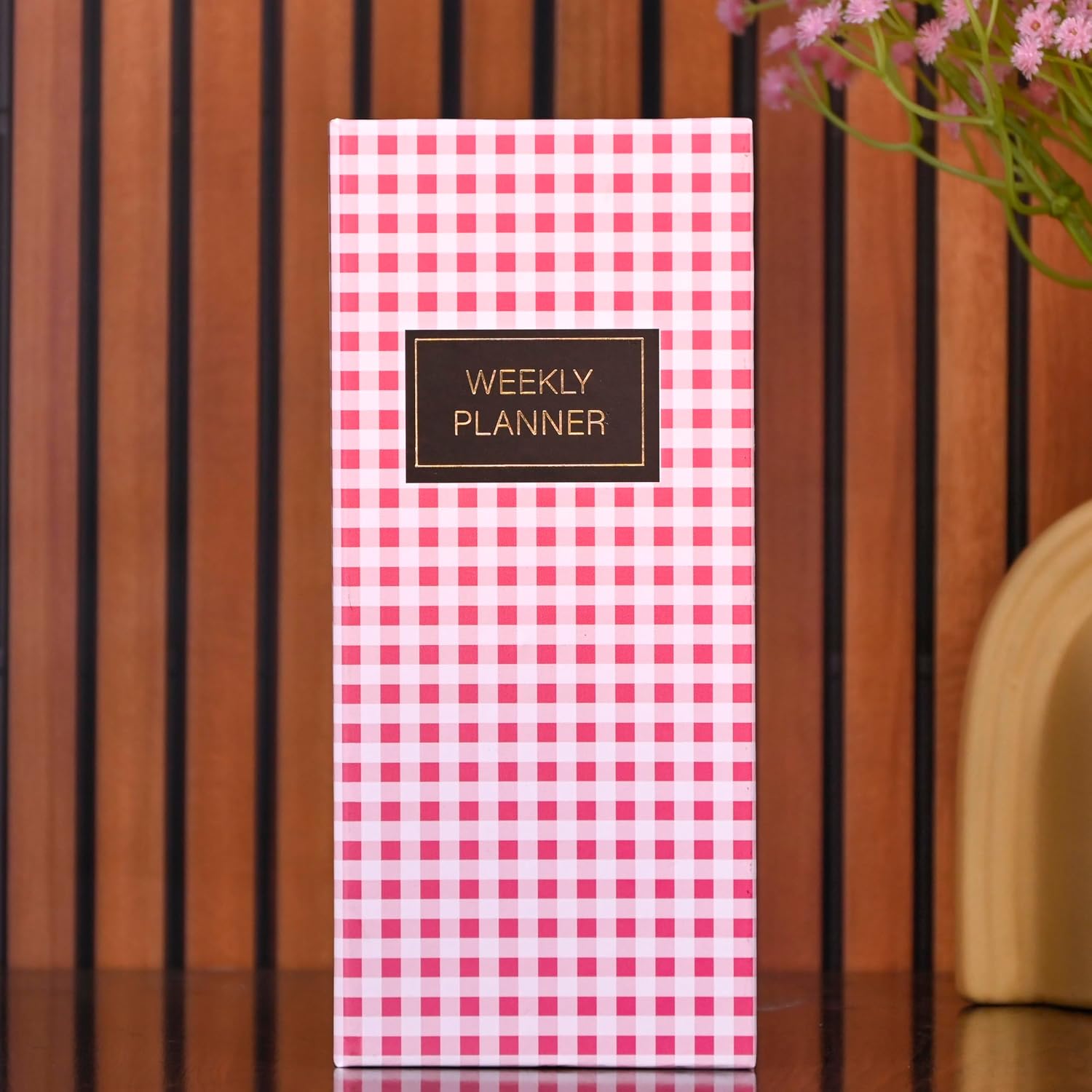 Weekly planner with pink checkered design on a wooden surface