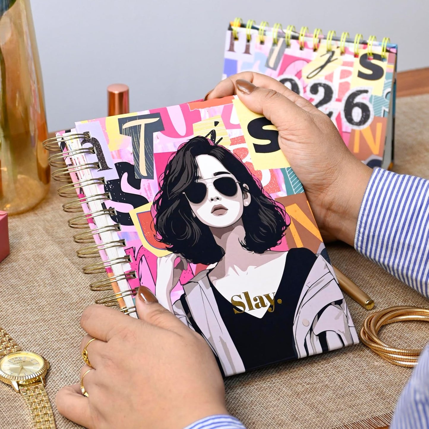 Person holding a colorful notebook with an illustration of a person wearing sunglasses and the word 'Slay'.